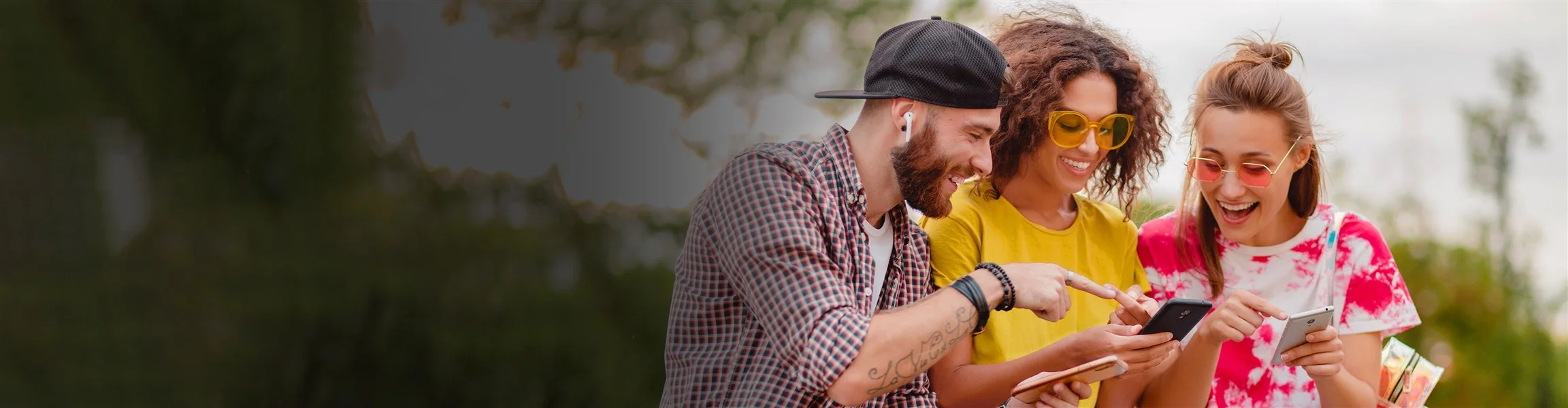 Muškarac i dvije djevojke veselog raspoloženja gledaju u mobitele